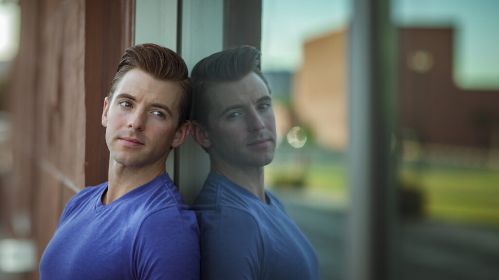 Handsome man in a blue shirt leaning against a reflective surface, captured by Rex Jones, showcasing portrait photography in Utah.