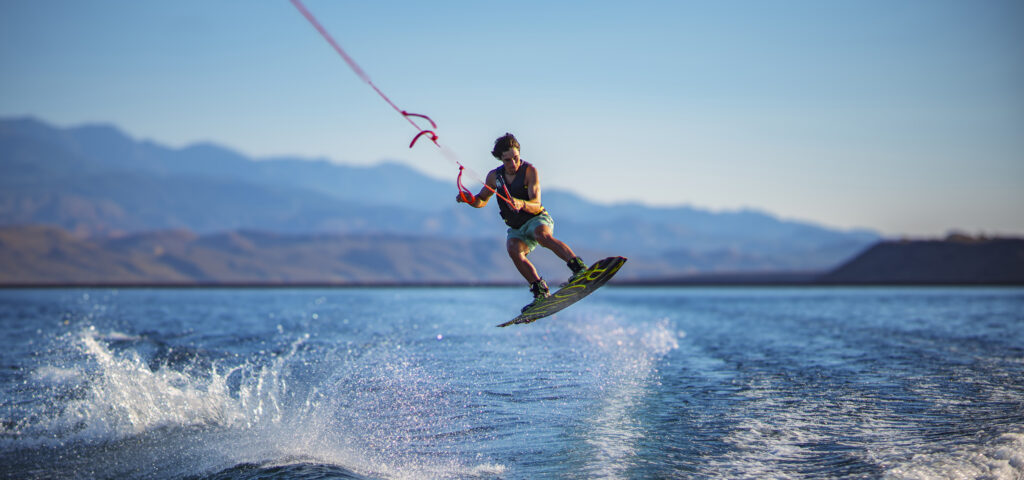 Wakeboarder performing a jump on a lake with a mountain backdrop, perfect for marketing photo and video campaigns highlighting summer adventure.